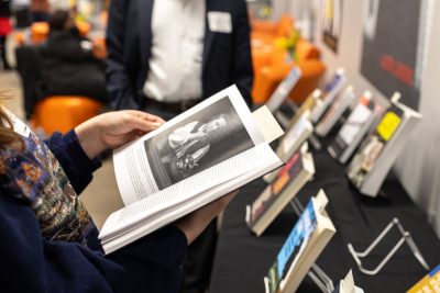 Someone is holding a book with other books on a shelf behind it.
