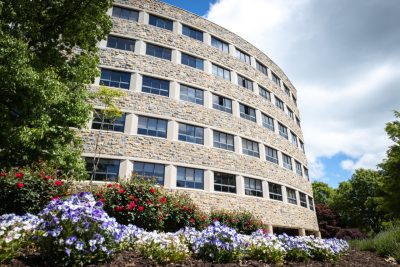 Newman Library's iconic curved building with purple and red flowers in front of it.