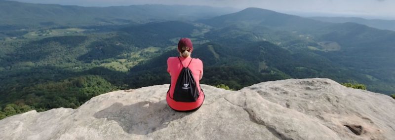 female student sitting atop a cliff overlooking the new river valley and  mountains